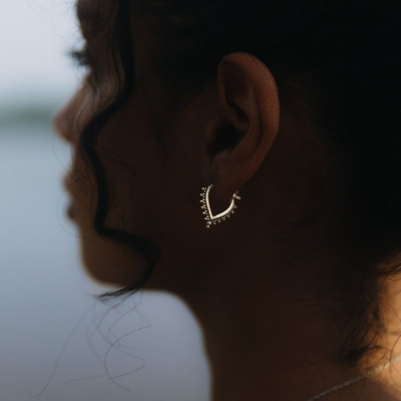 925 sterling silver V-shaped hoop earring with granulated bead detailing along the arch, worn close to the ear on a model.
