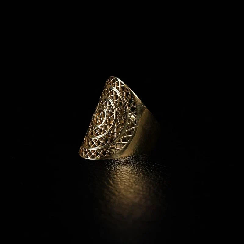 Handcrafted brass statement ring with open lattice filigree face and central sun motif, photographed against a black background.