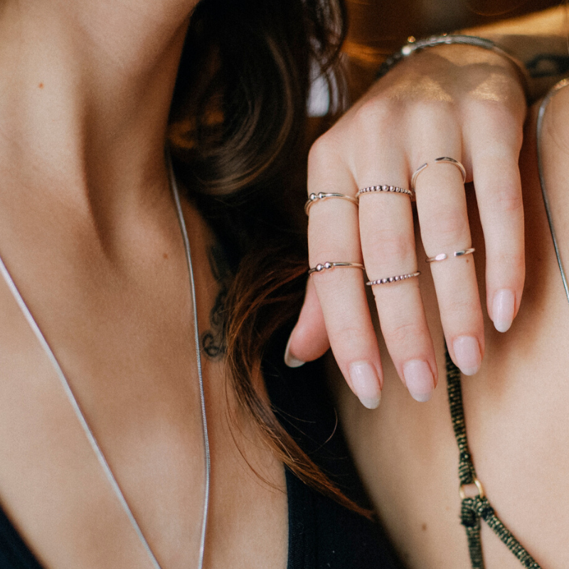Hand wearing a stacked set of slim minimalist rings in 925 sterling silver alongside layered silver necklace chains.