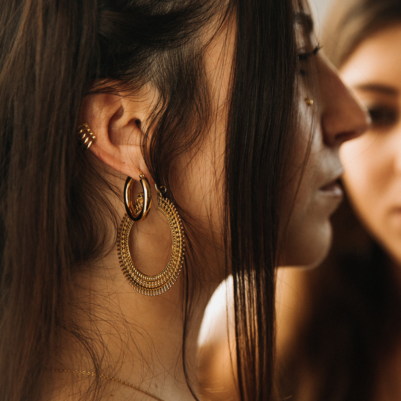 Gold hoop earrings layered with an ear cuff, worn against dark hair