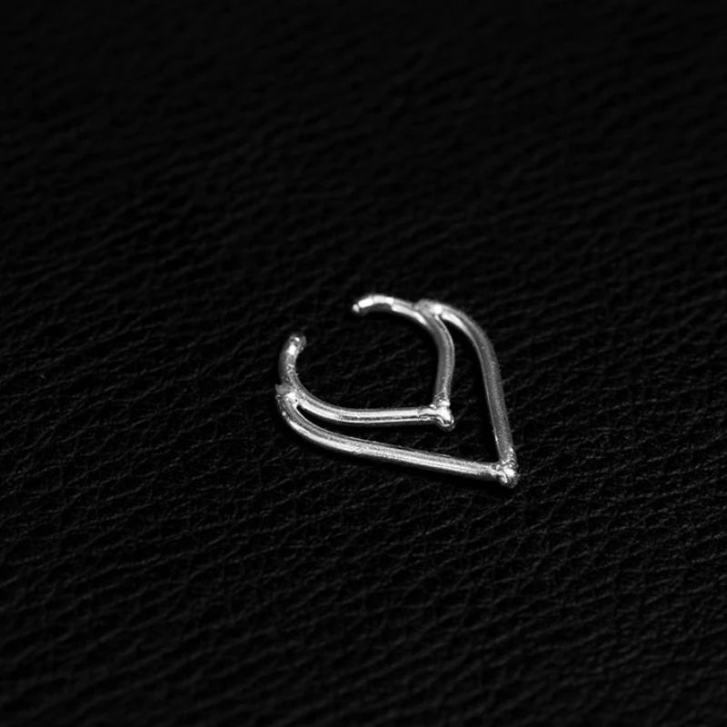 Silver septum ring shaped as a doubled chevron, two slim wires meeting in a soft downward point, resting on black textured leather