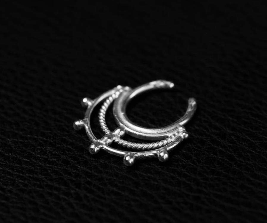 Silver septum ring shaped as a doubled chevron, two slim wires meeting in a soft downward point, resting on black textured leather